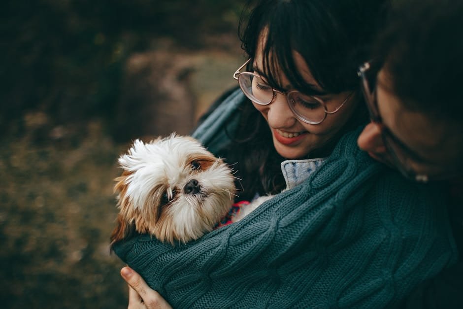 A woman lovingly cuddles her Shih Tzu puppy, wrapped in a warm blanket outdoors.