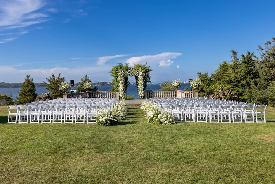 Best Insurance in Rhode Island 2025 02/22/2026 Beautiful outdoor wedding setup by the water with white chairs and floral arch in Newport, RI.