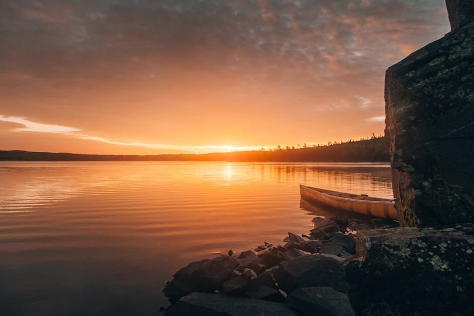 A tranquil sunset over a lake in Ely, Minnesota, featuring a canoe by the rocky shore.