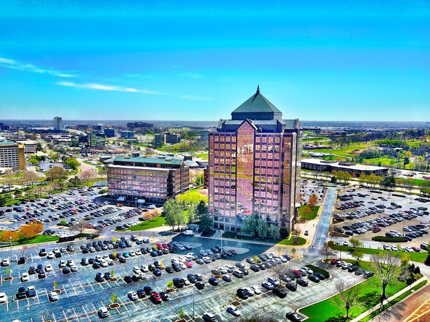Bird's-eye view of a modern skyscraper and parking lot in Overland Park, KS, under a clear blue sky.