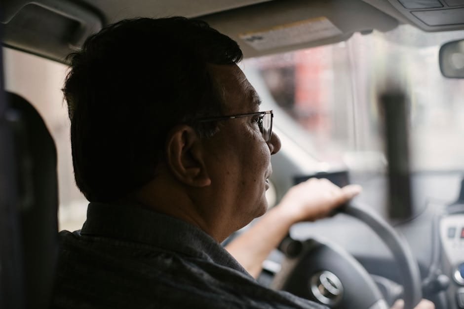 Side view of focused aged male with glasses driving automobile on street on urban background in soft daylight