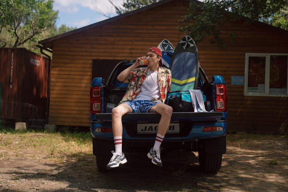 Teenager enjoying a drink on a pick-up truck outside a cabin, surrounded by nature.